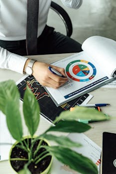 Business professional analyzing financial graphs and charts at an office desk with a laptop.
