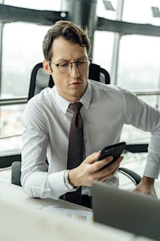 Caucasian man in office attire checking his smartphone, symbolizing modern work communication.
