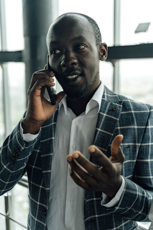 Free African American man in a suit talking on a smartphone indoors with city view. Stock Photo
