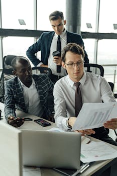 Three business professionals discuss documents in a bright modern office setting.