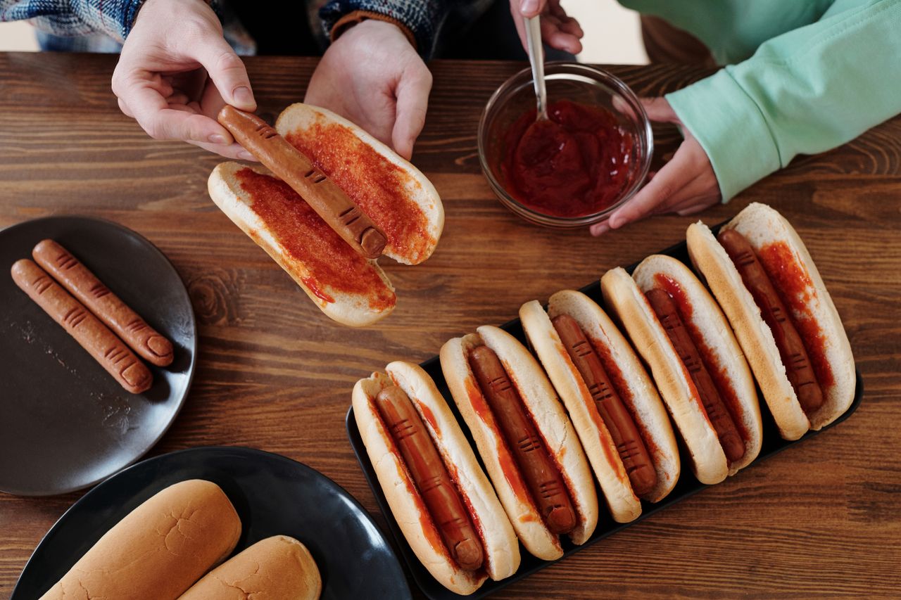 Hands preparing hot dogs with ketchup to look like fingers