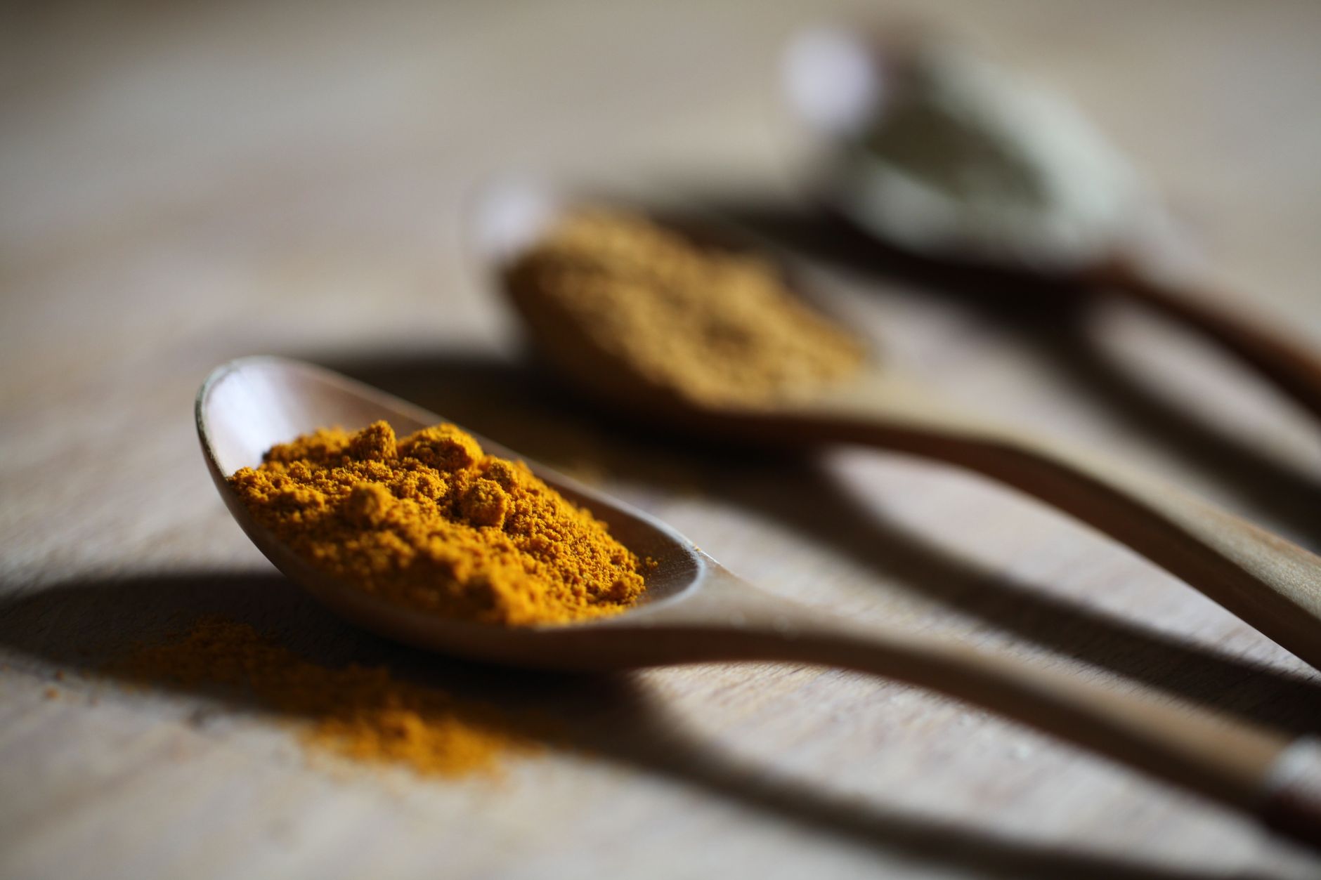 Vibrant turmeric powder on a wooden spoon with a blurred background for culinary use.