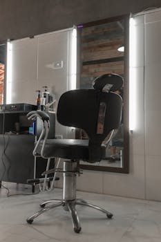 A stylish barbershop chair in front of a mirror with illuminated lights.