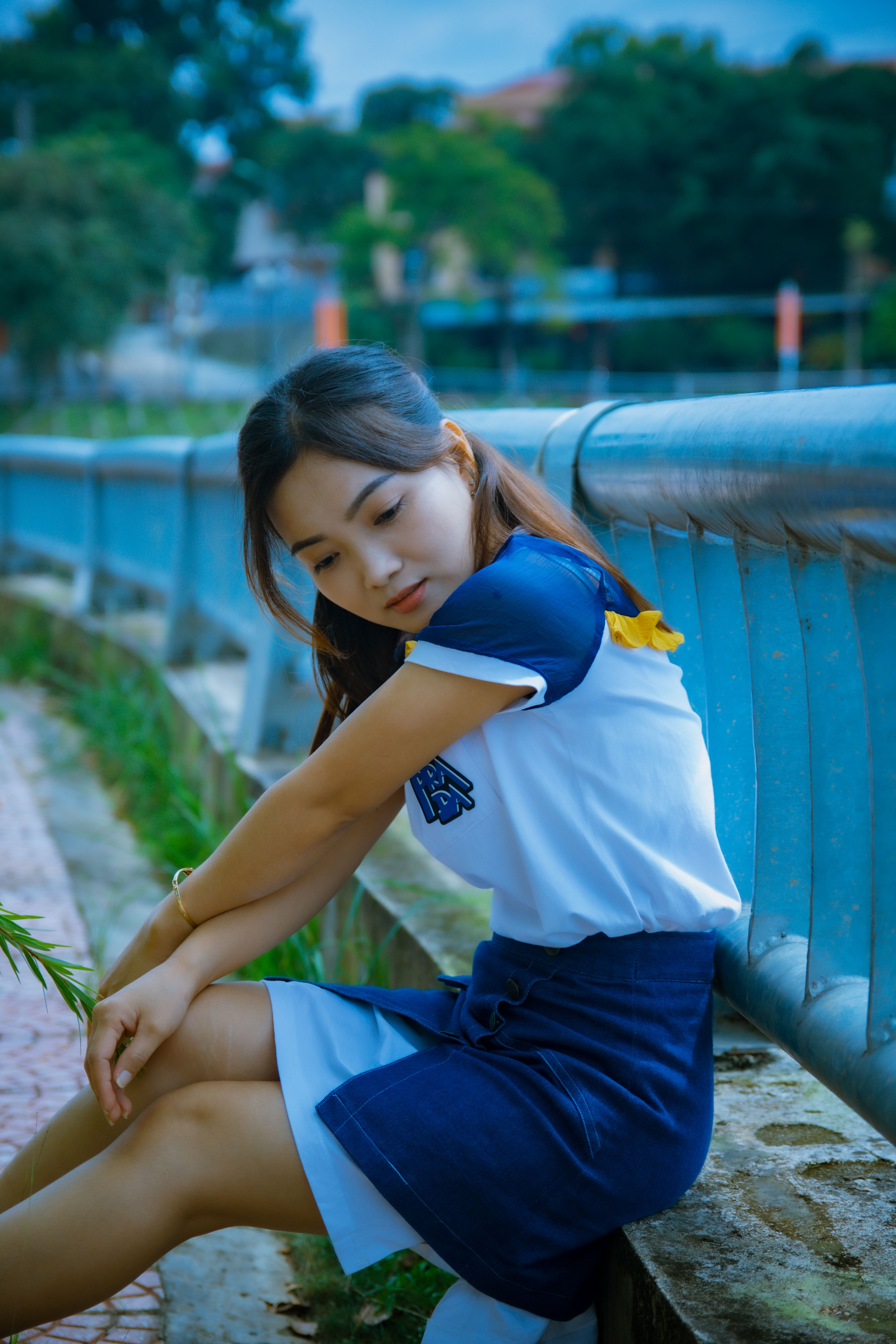 一位年轻女子独自坐在户外的金属栏杆旁，若有所思地向下凝视