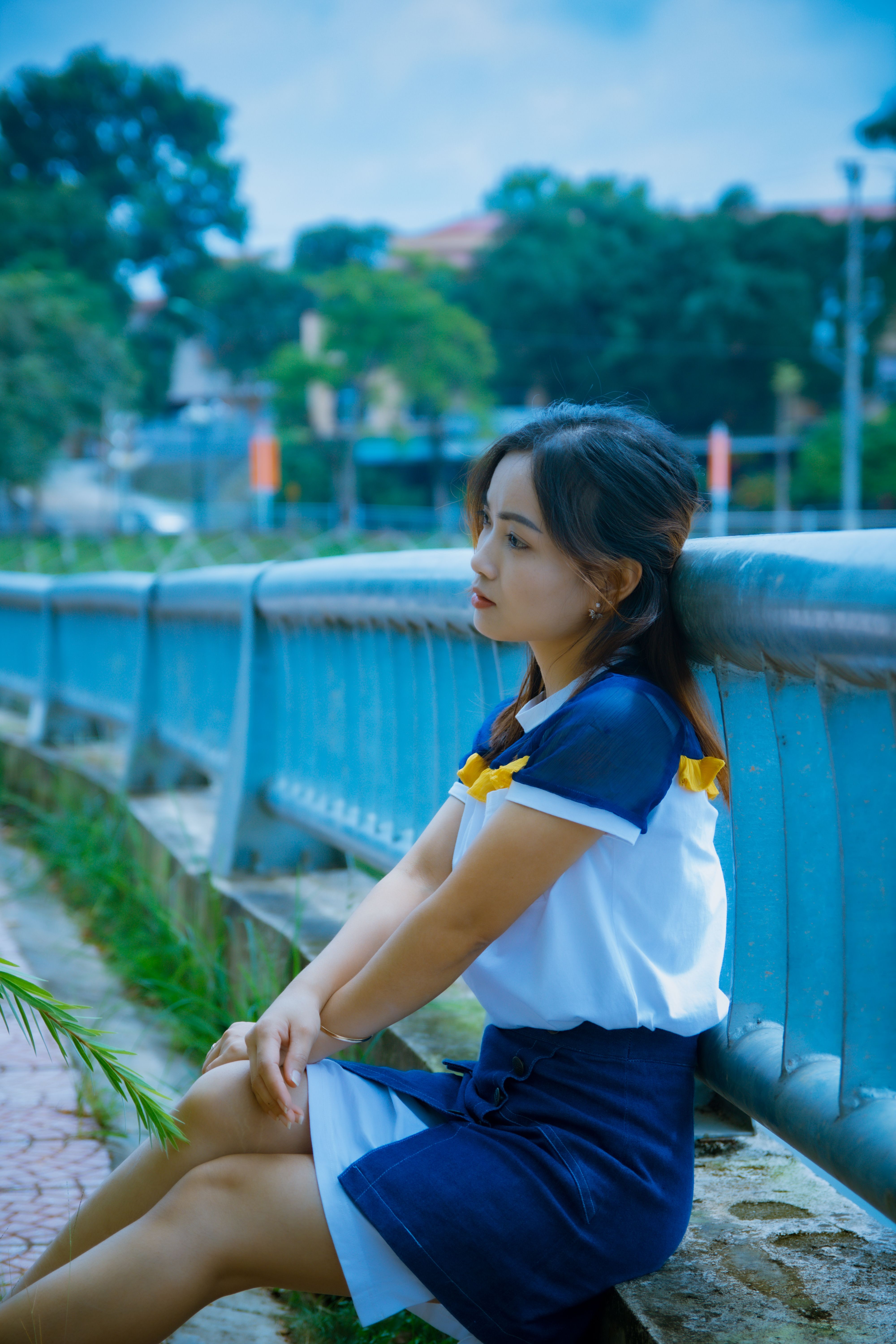 一位沉思的女人独自坐在宁静城市环境中的蓝色栏杆旁