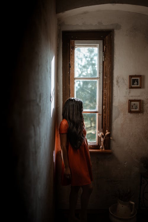 Anonymous woman standing near window in shabby wall
