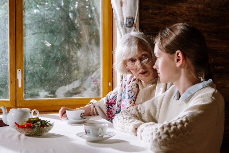 An Elderly Woman Sitting At A Table With A Young Woman