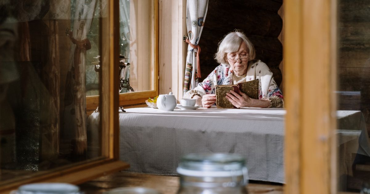 Woman enjoying tea and reading by a window in a cozy cabin