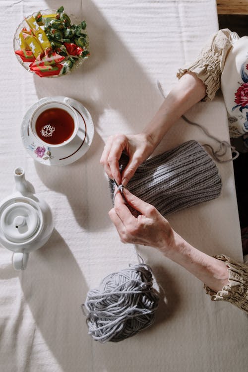 Person Holding a Knitwork Beside a Cup of Tea