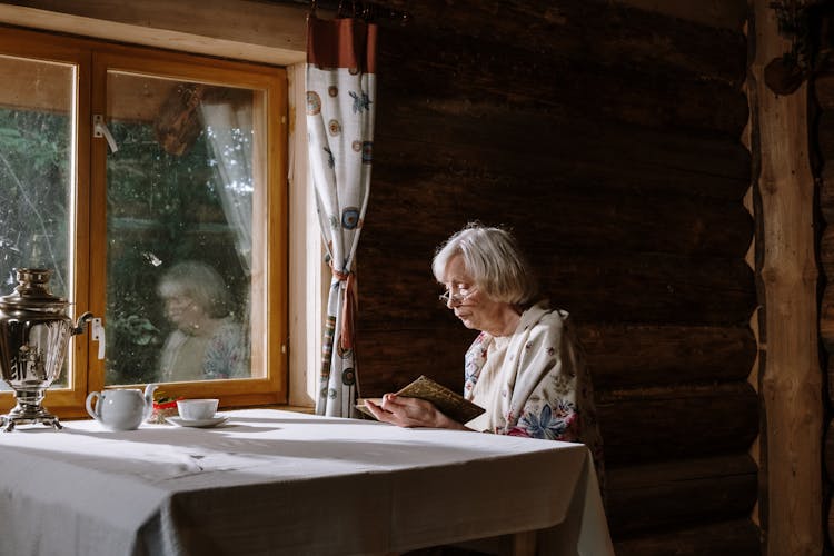 An Elderly Woman Reading A Book At Home