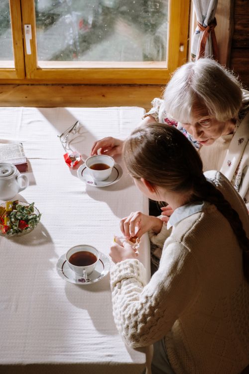 Free A heartwarming moment of a grandmother and granddaughter sharing tea indoors on a sunny day. Stock Photo