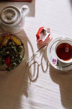 在阳光明媚的午后，桌上摆放着茶水、糖果和眼镜，自上而下看去，营造出舒适的氛围