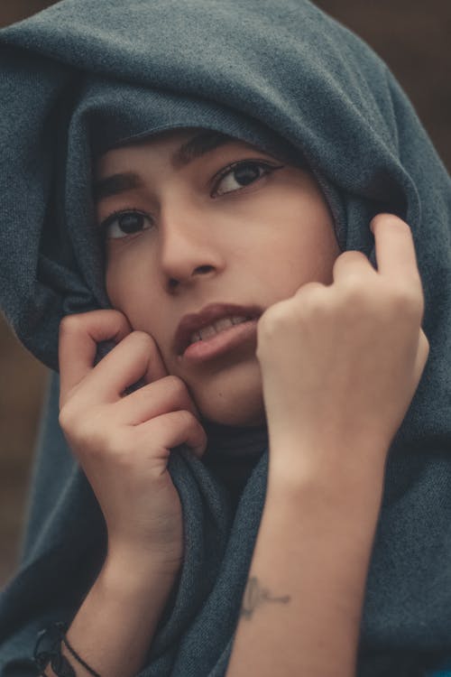 Pensive woman touching headscarf with mouth opened