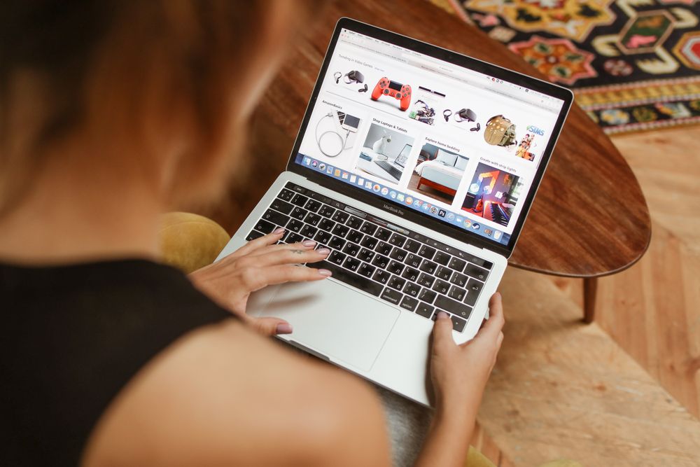 A woman shops online on her laptop while seated in a cozy home environment