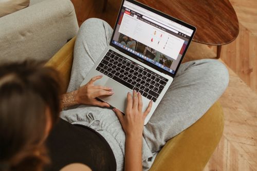 Free A person leisurely shopping online from home, using a laptop while sitting on a cozy chair. Stock Photo