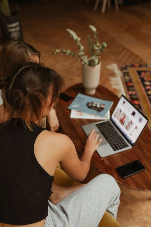 Free Two women sitting together, browsing online shopping websites on a laptop indoors. Stock Photo