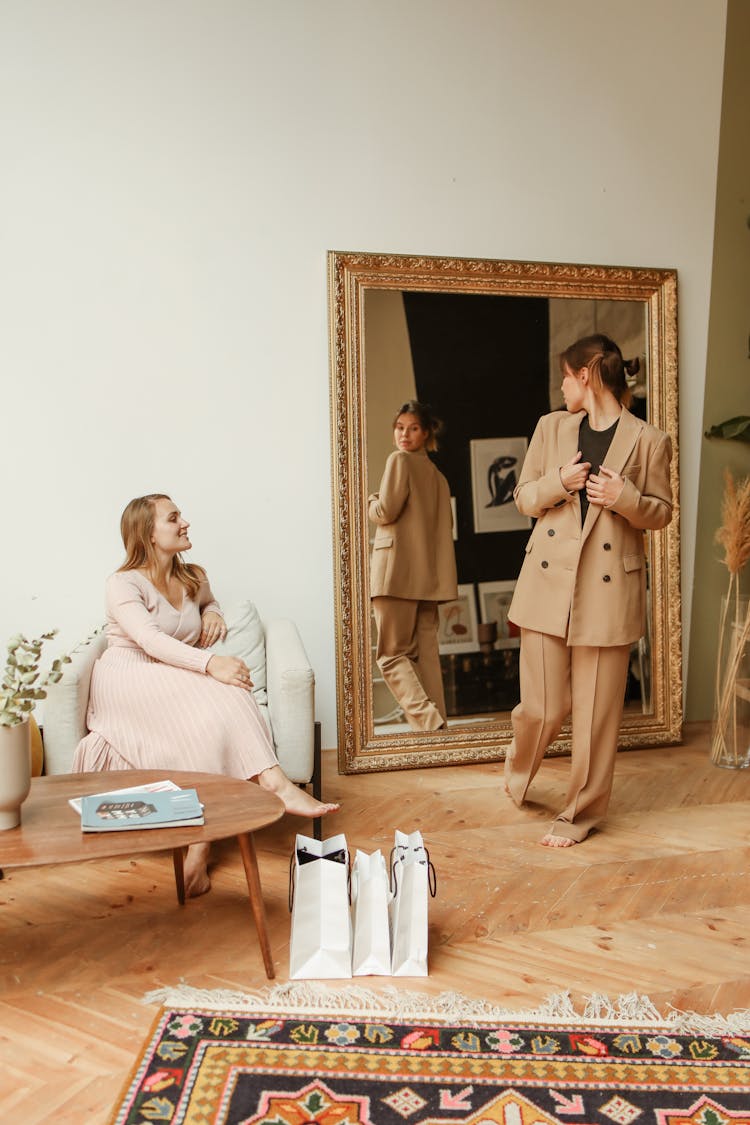 Woman Looking At Her Outfit In A Mirror And Her Friend Sitting In An Armchair 