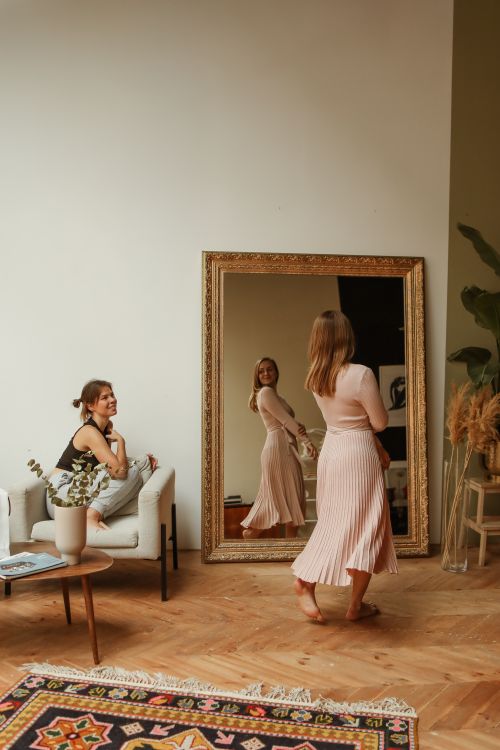 Free Woman admiring dress in mirror with natural light interior setting. Stock Photo