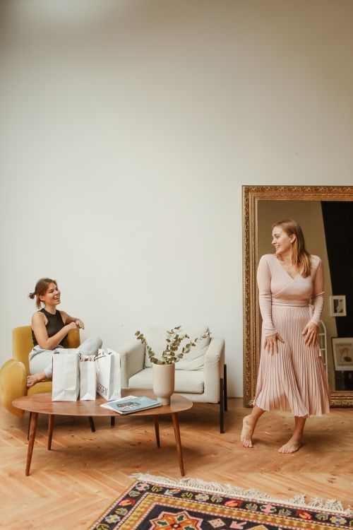 Free Two women in a cozy room, one in a beige dress, relaxing and trying on outfits. Stock Photo