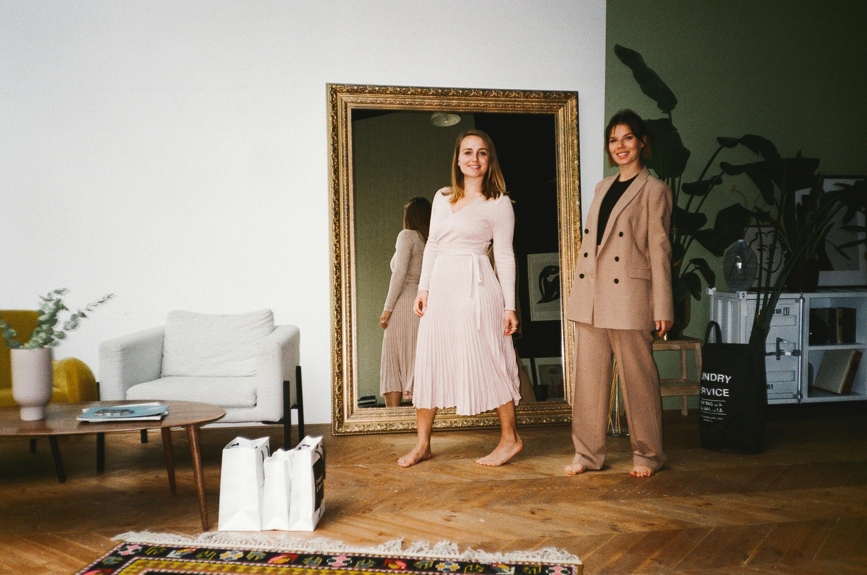 两个女人赤脚站在室内，微笑着映照在镜子中