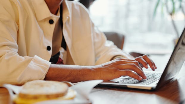 Close-up of hands typing on a laptop keyboard in a warm indoor environment with soft lighting.