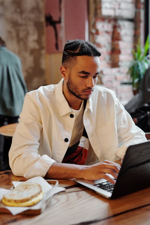 Free Young man focused on work with laptop in a stylish cafe setting, exuding concentration and modern style. Stock Photo