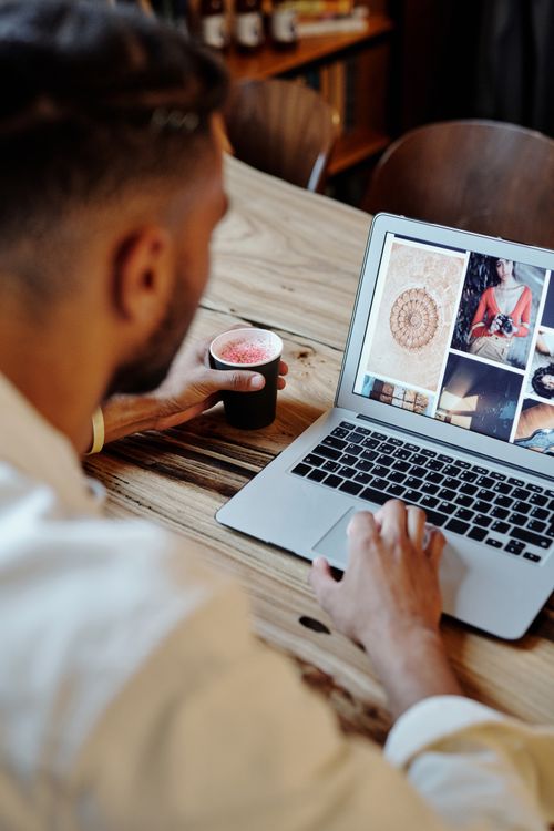 Free Man focused on work on laptop with artistic images and coffee in a cozy setting. Stock Photo