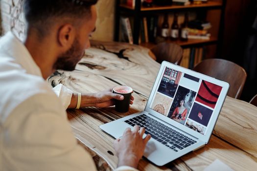 A young man working on his laptop in a stylish cafe, sipping coffee and focused on his tasks.