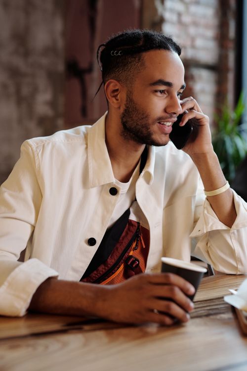 Free Young man in casual clothes enjoying a phone call while holding a coffee cup indoors. Stock Photo