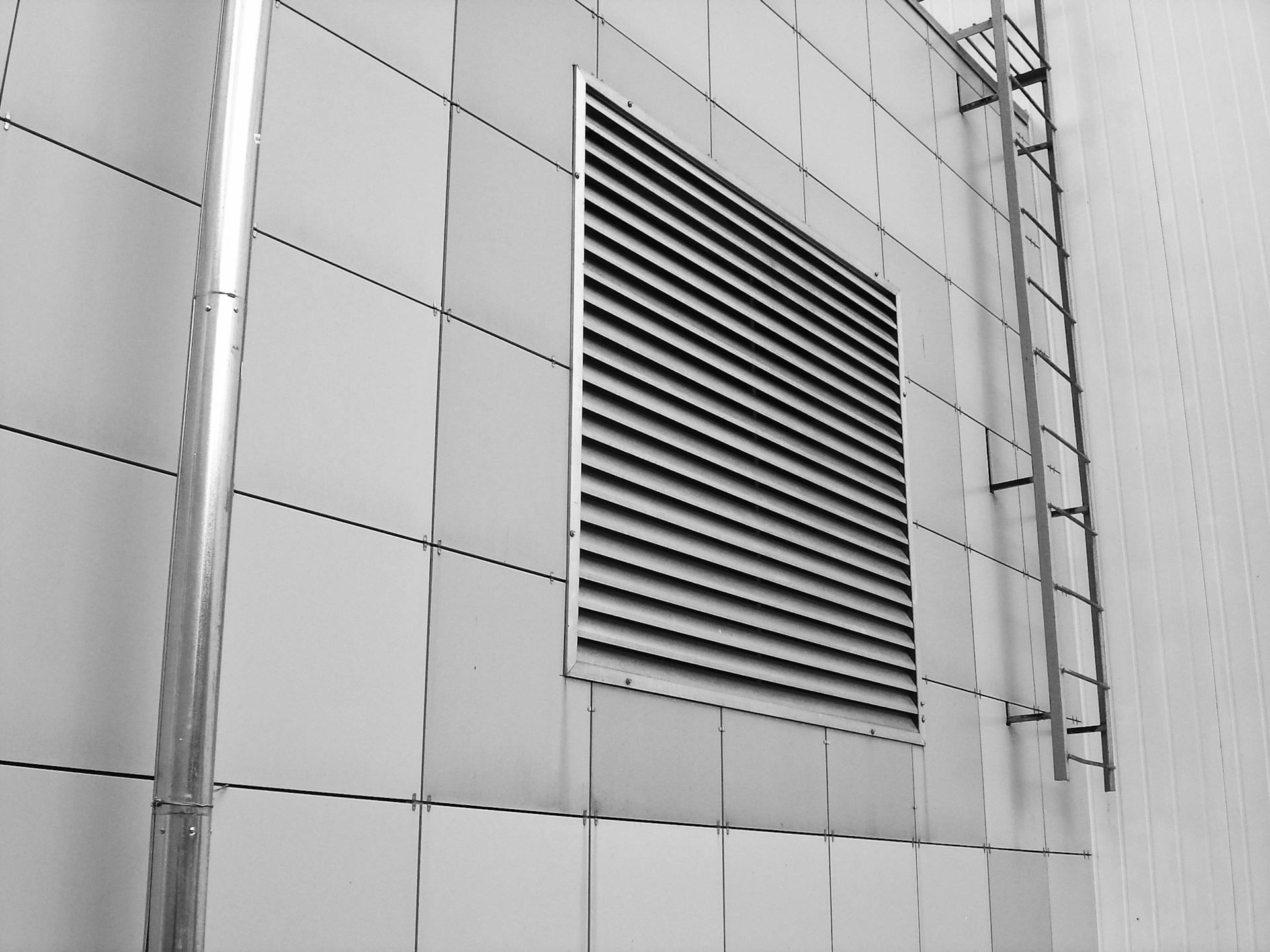 Close-up of a modern building exterior showing a ventilation system and metal ladder.