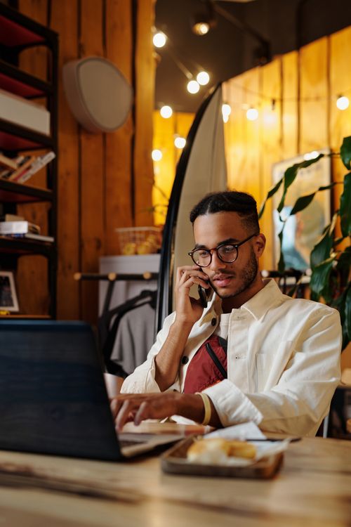 Free A stylish freelancer multitasking on phone and laptop in a cozy, well-lit café. Stock Photo