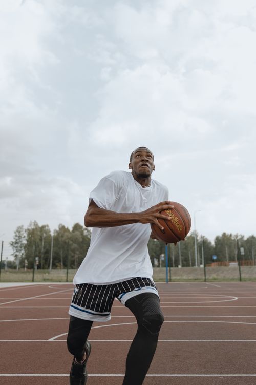 Free A focused athlete in activewear prepares for a layup on an outdoor basketball court under cloudy skies. Stock Photo