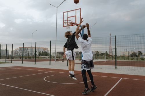 Free Dynamic shot of two athletes playing basketball on an urban outdoor court during the day. Stock Photo