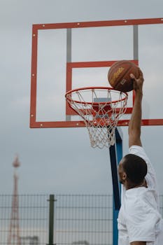 An energetic basketball player dunks on an outdoor court hoop.