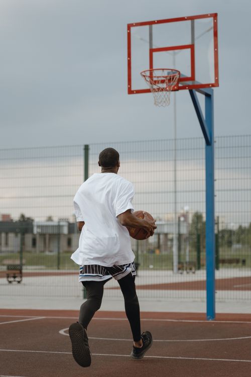 Free Rear view of a man playing basketball on an outdoor court, aiming for a score. Stock Photo