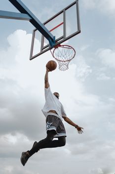 A basketball player in midair performing an impressive dunk against a backdrop of clouds.