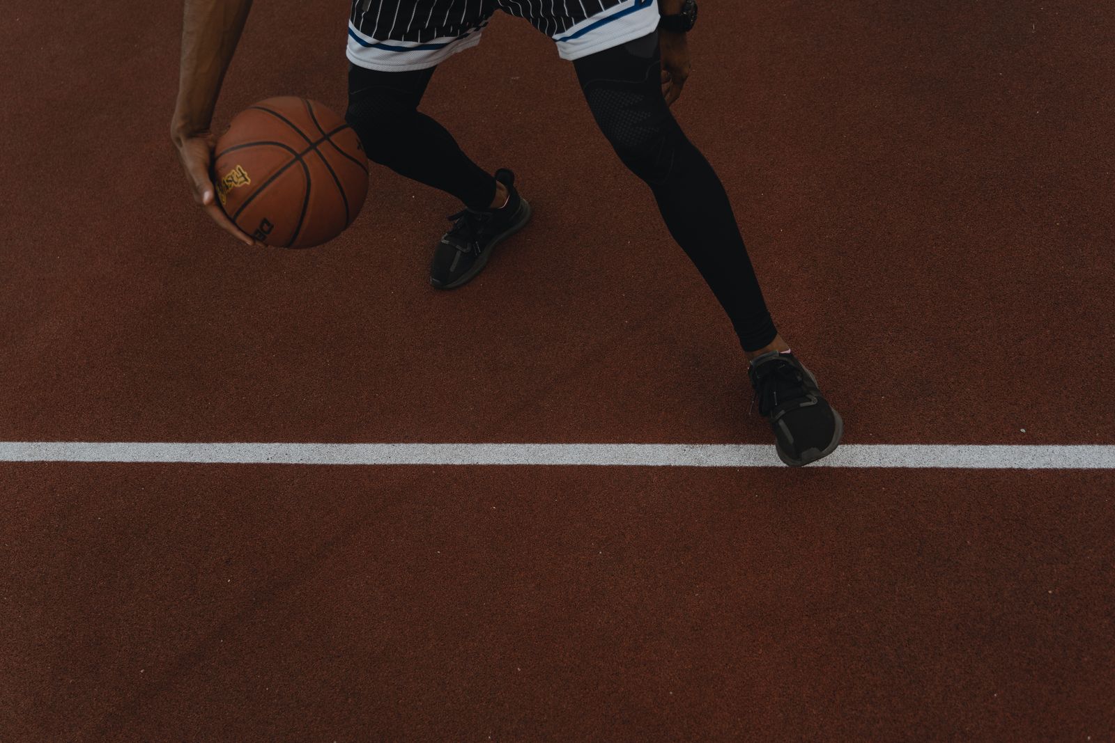 Atleta driblando a bola de basquete em quadra ao ar livre durante o dia