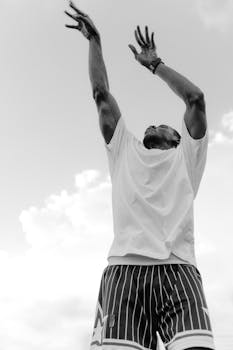 Black and white image of an athlete jumping and reaching high, illustrating energy and motion.