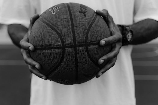 A monochrome image capturing hands firmly gripping a basketball on a court.