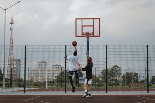 Free Two adults playing basketball on an outdoor court during the day, attempting a jump shot. Stock Photo