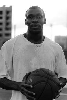 Black and white photo of a man holding a basketball outdoors with blurred urban background.