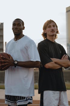 Two adult men standing outdoors back-to-back on a basketball court, expressing friendship.