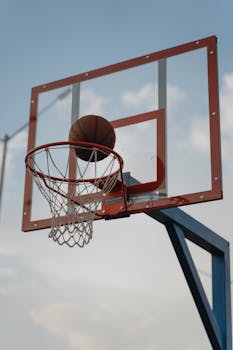 A basketball midair aiming for the hoop with a clear sky backdrop.