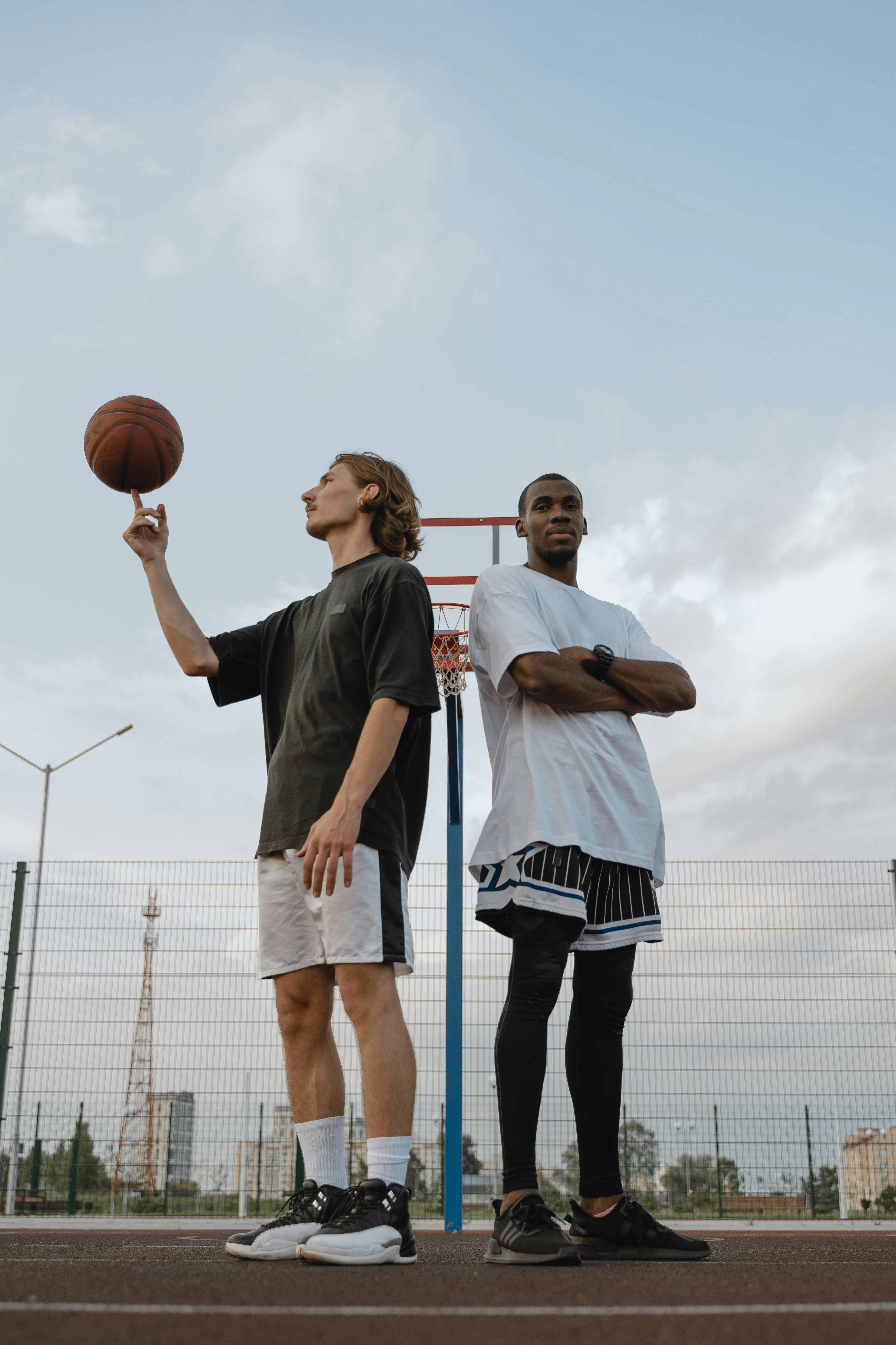Two young men on an outdoor basketball court, one spinning a ball on his finger.