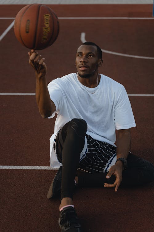 Man in White Crew Neck T-shirt Doing Trick with Basketball 