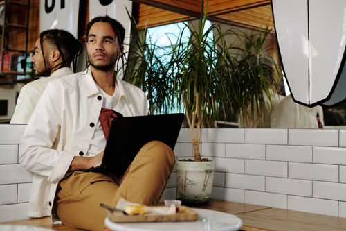 Free Contemporary young man with afro braids using laptop indoors, reflecting thoughtful mood. Stock Photo