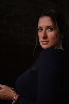 Elegant portrait of a woman in a dark, moody setting, highlighting her serene expression and stylish attire.