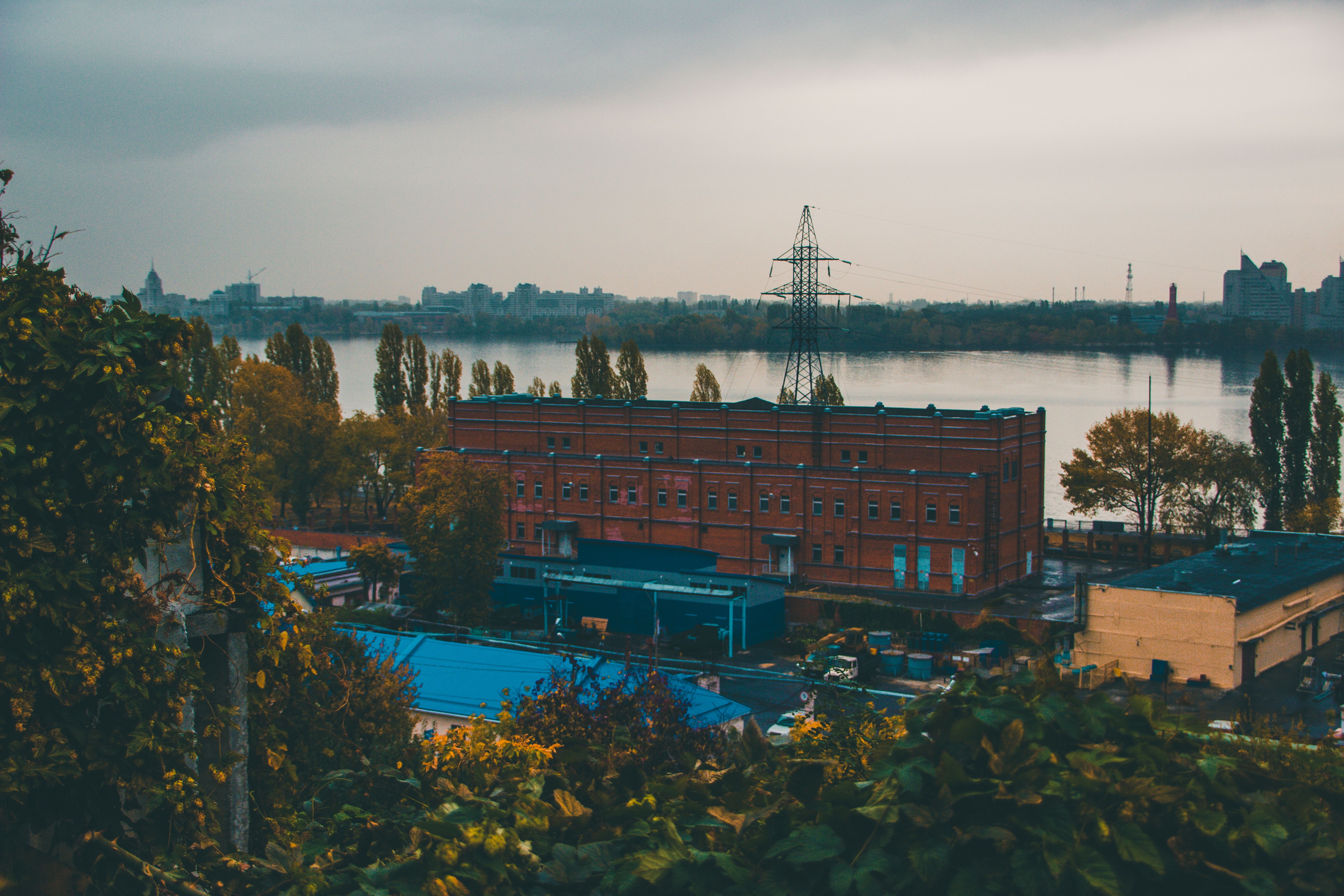 A gloomy urban landscape featuring a red brick industrial building near a river.
