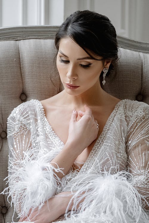 Sensitive young bride in posh white dress sitting on sofa