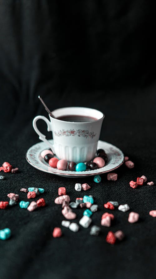 From above of aromatic coffee in porcelain cup with spoon and bright sweets on saucer and table